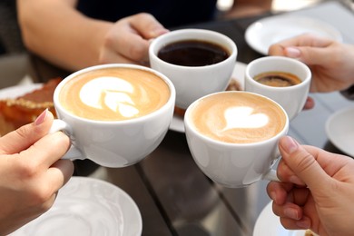 Photo of Friends drinking coffee at wooden table in outdoor cafe, closeup