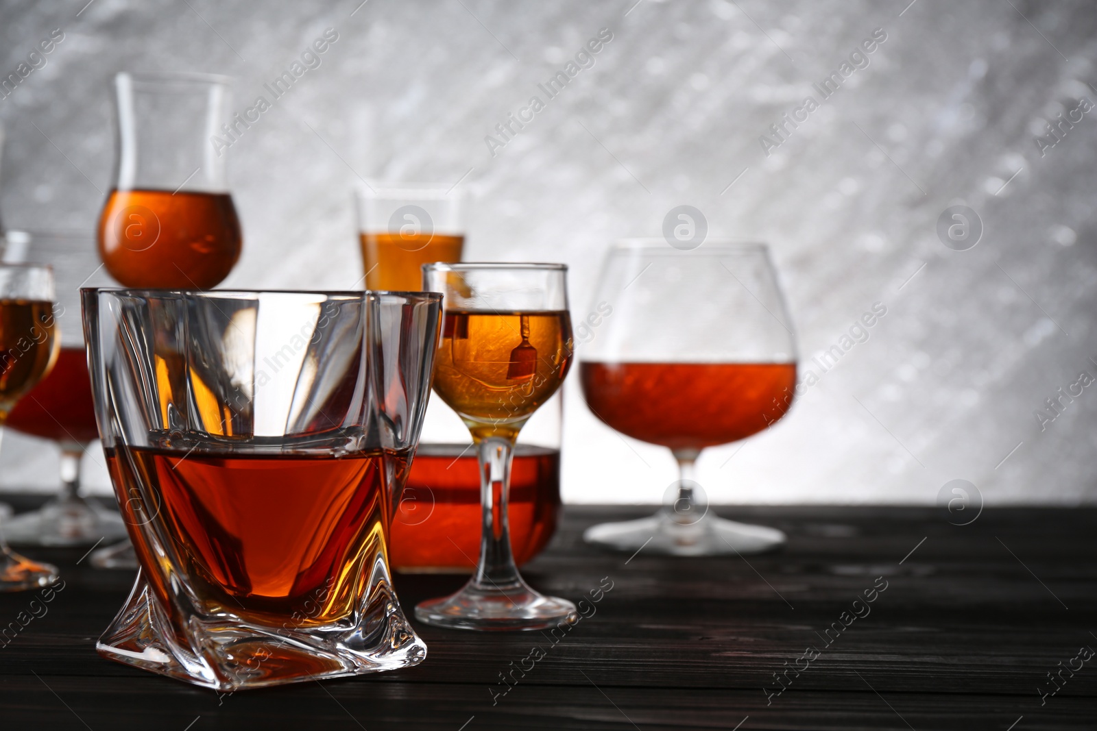 Photo of Different delicious liqueurs in glasses on dark wooden table, space for text