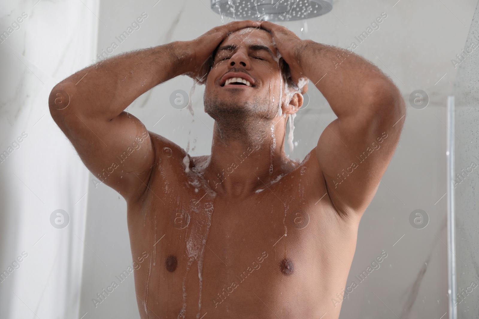 Photo of Handsome man washing hair in shower at home