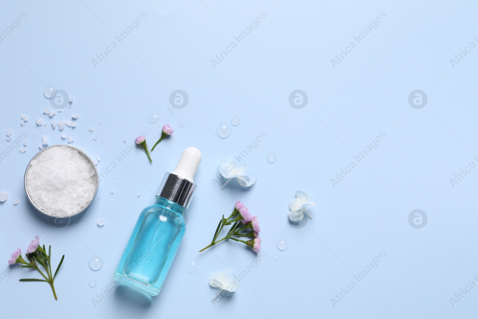 Photo of Bottle of cosmetic serum, beautiful flowers and sea salt on light blue background, flat lay. Space for text