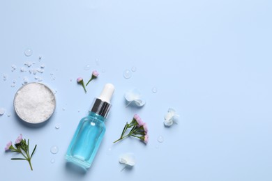 Bottle of cosmetic serum, beautiful flowers and sea salt on light blue background, flat lay. Space for text