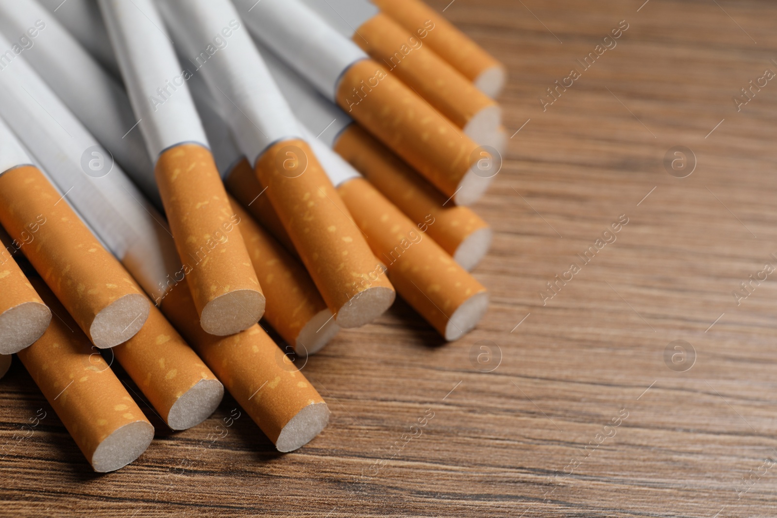 Photo of Pile of cigarettes on wooden table, closeup. Space for text