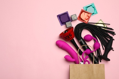 Photo of Shopping bag and different sex toys on pink background, flat lay. Space for text