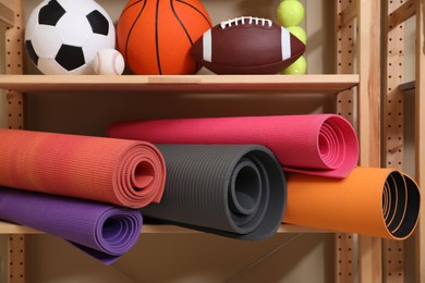 Photo of Different sport balls and yoga mats on rack indoors