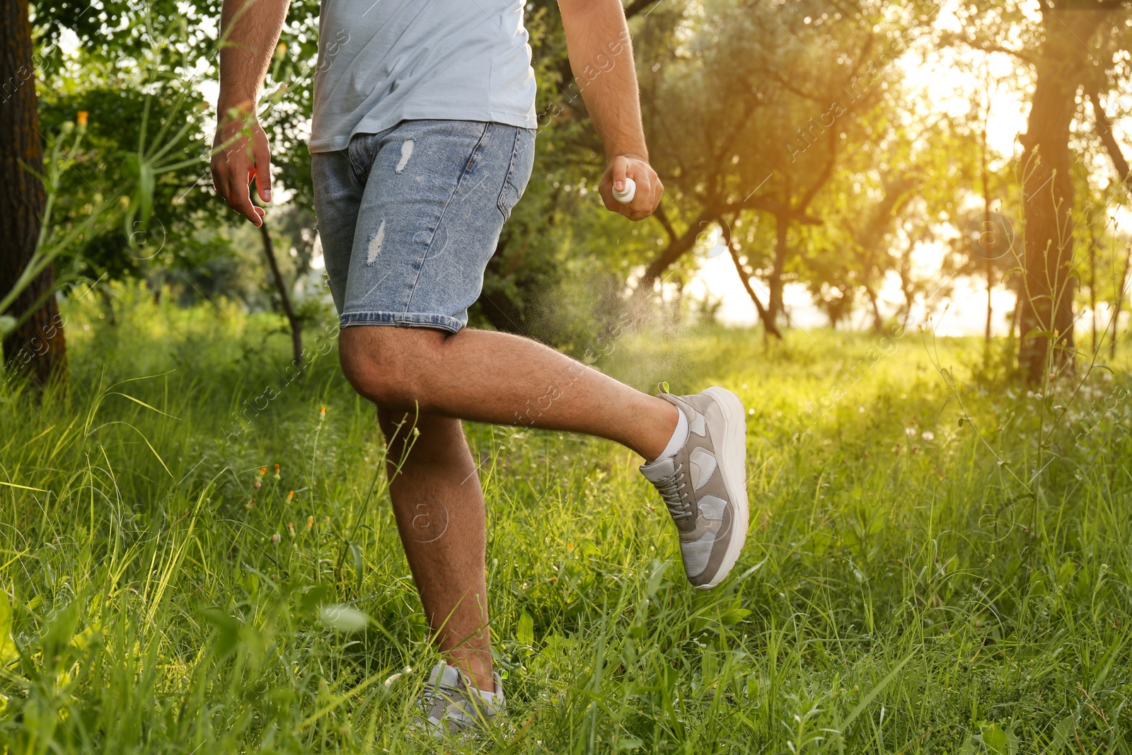 Photo of Man applying insect repellent on leg in park, closeup. Tick bites prevention