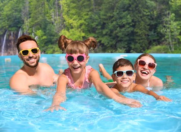 Image of Happy family having fun in outdoor swimming pool at luxury resort on sunny day