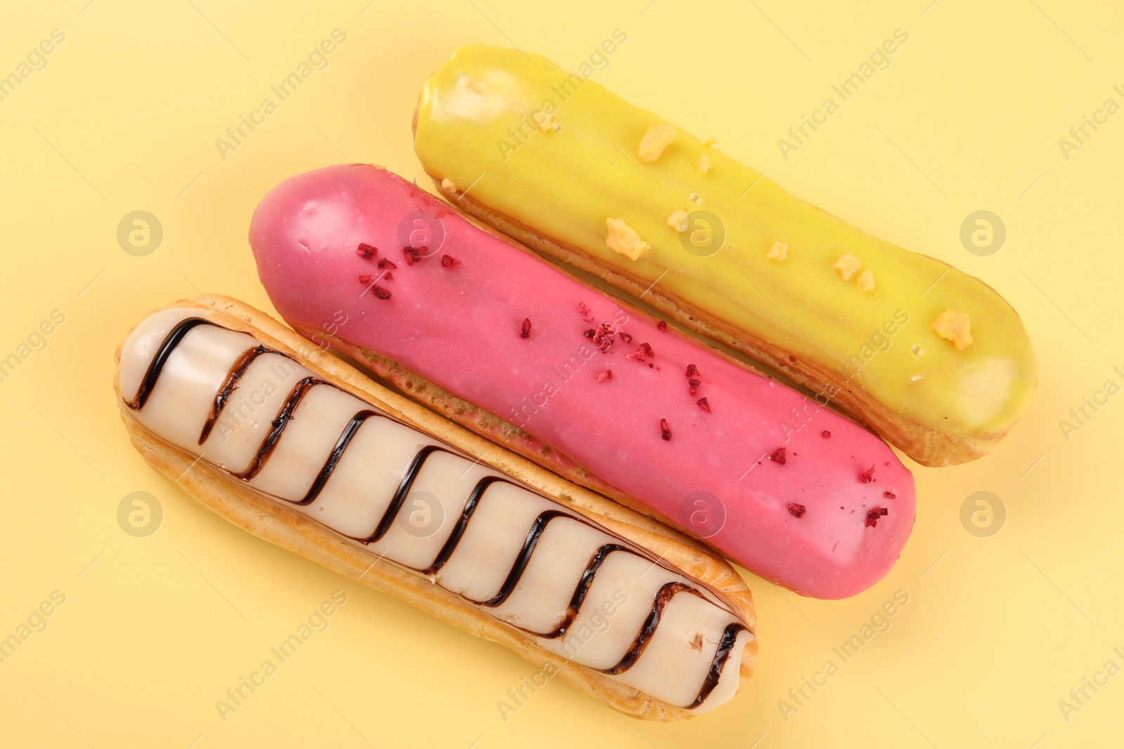 Photo of Delicious eclairs covered with glaze on yellow background, top view