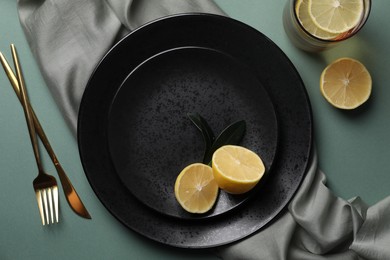 Stylish table setting. Plates, cutlery and tea with lemon on olive background, flat lay