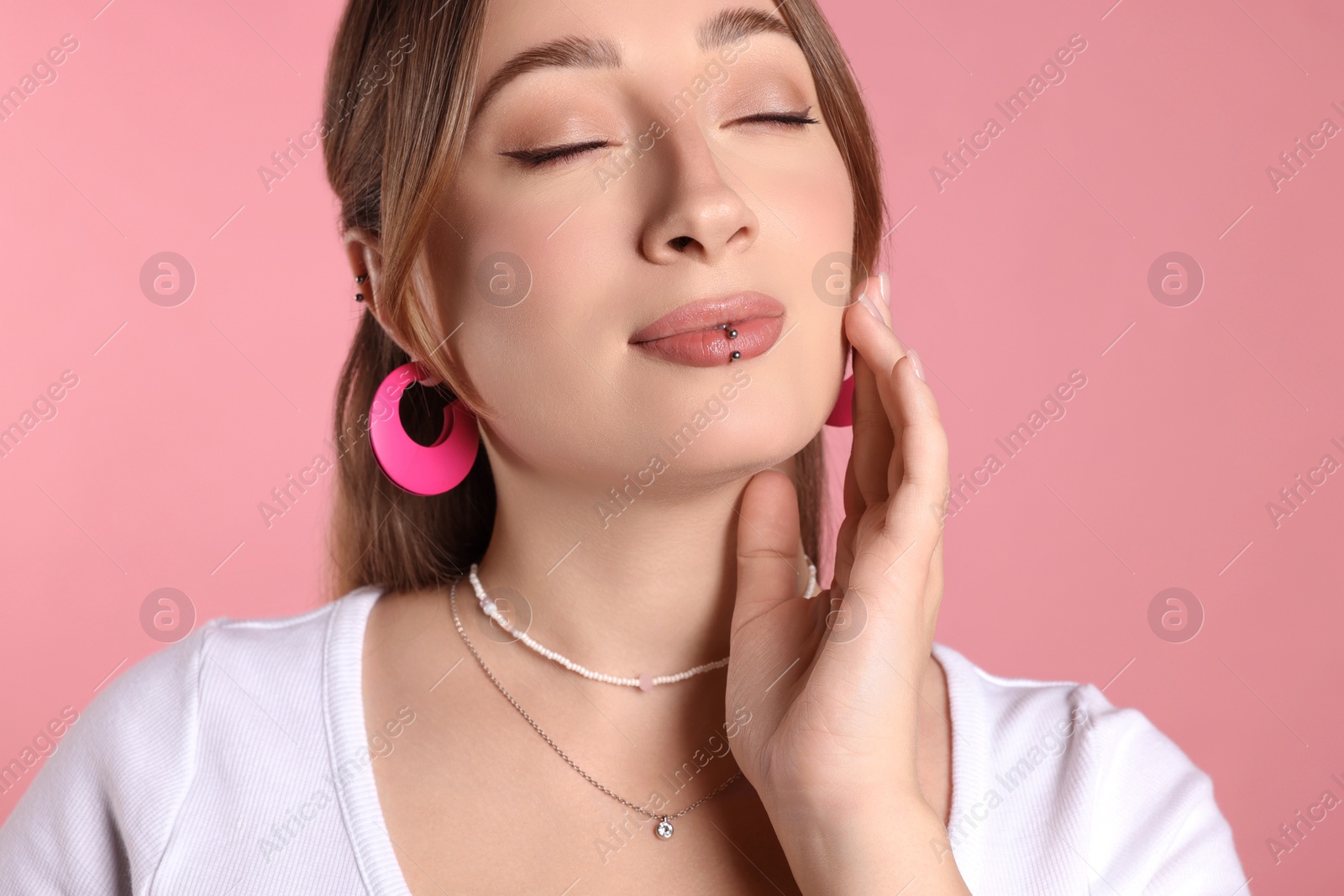 Photo of Young woman with lip and ear piercings on pink background, closeup