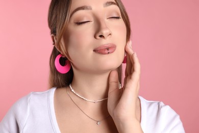 Photo of Young woman with lip and ear piercings on pink background, closeup