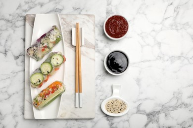 Different delicious rolls wrapped in rice paper on white marble table, flat lay. Space for text