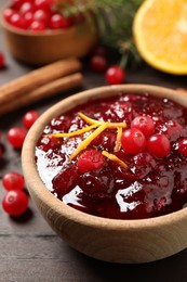 Cranberry sauce with orange peel on wooden table, closeup
