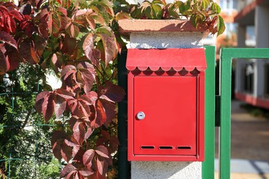Red metal letter box on stone column near gate outdoors