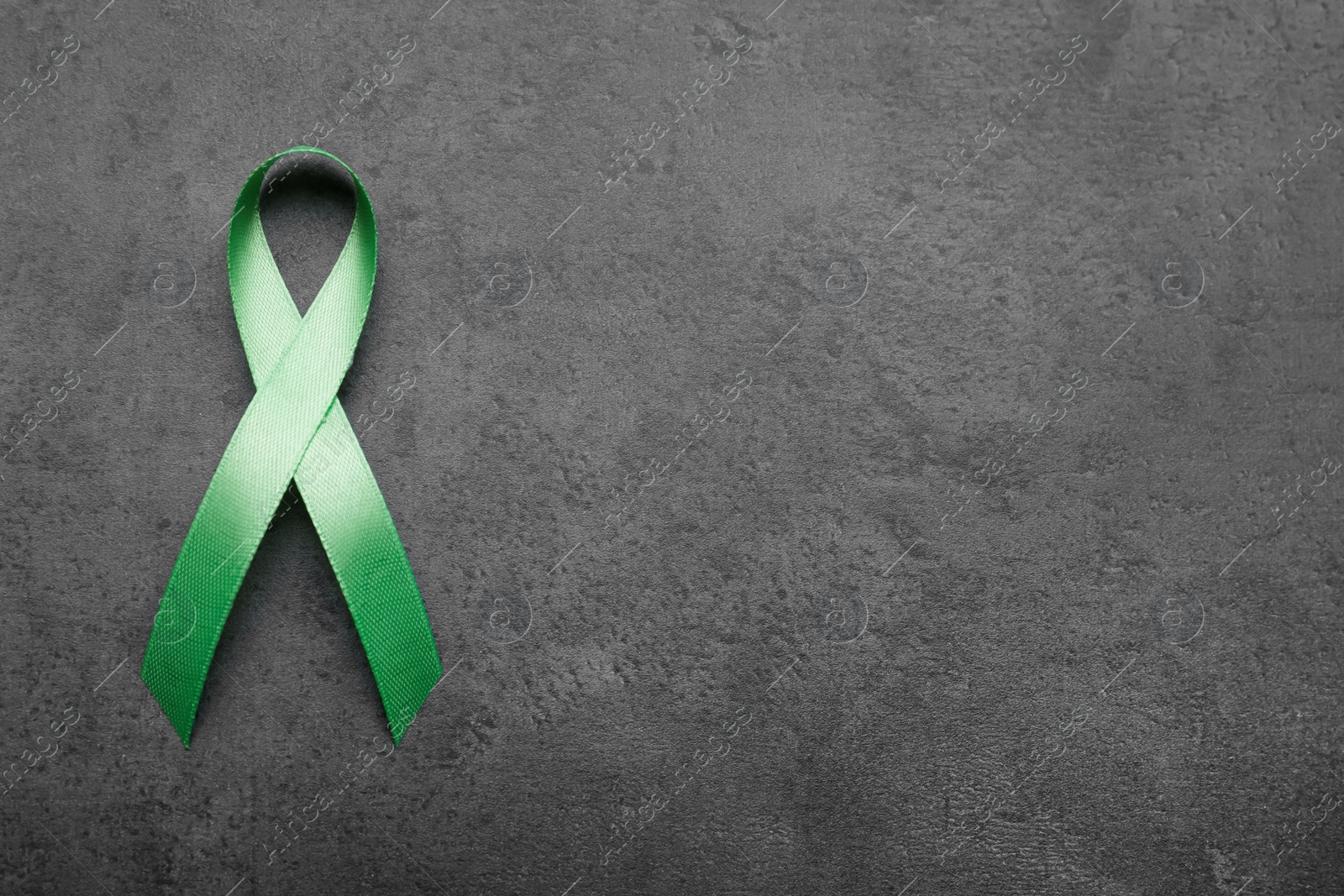 Photo of World Mental Health Day. Green ribbon on black background, top view with space for text