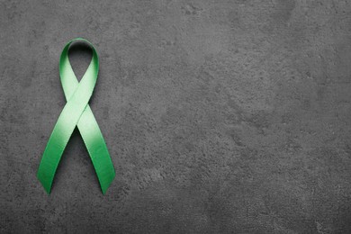 Photo of World Mental Health Day. Green ribbon on black background, top view with space for text