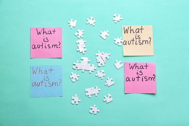 Photo of Sticky notes with phrase "What is autism?" and puzzle pieces on color background, flat lay