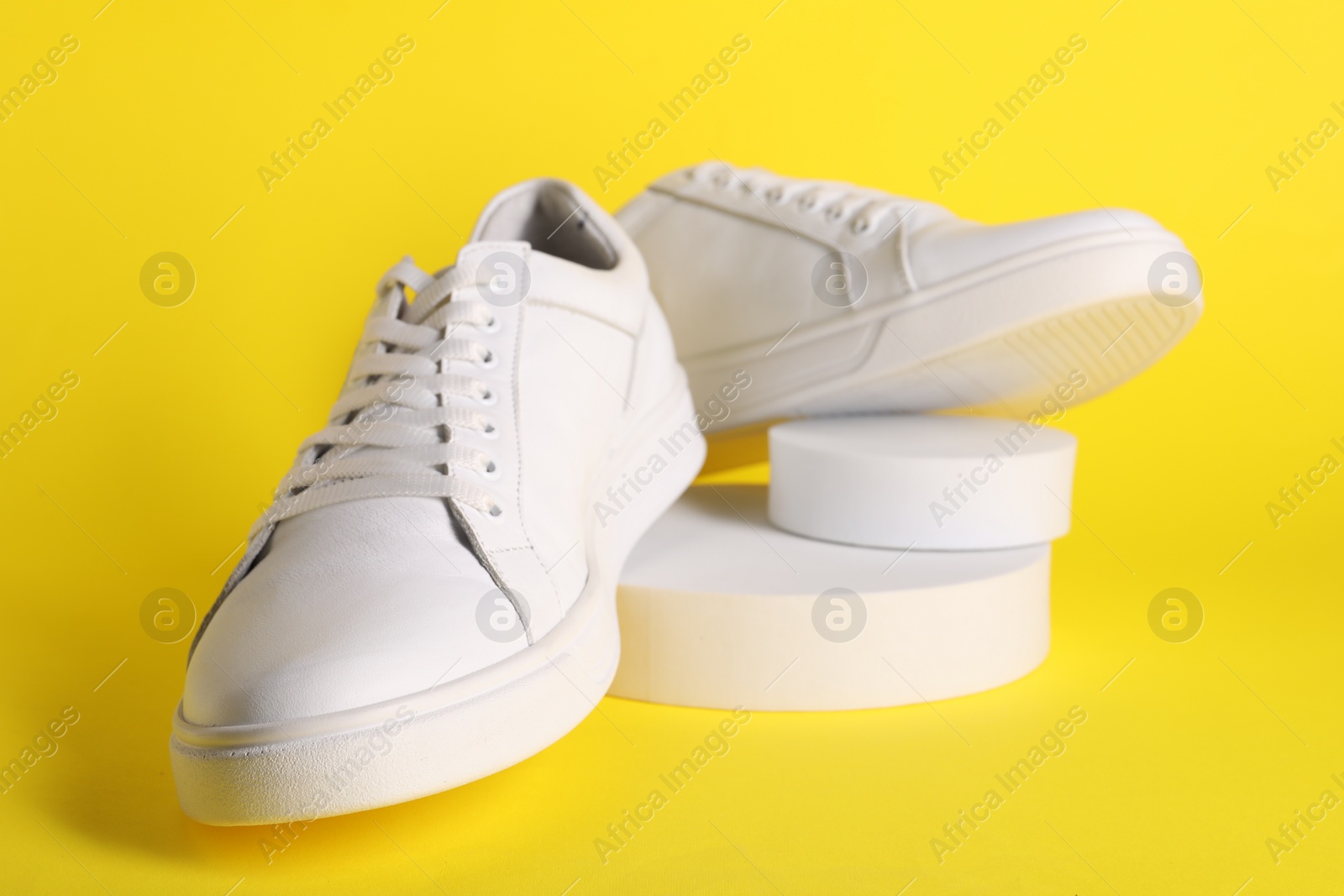 Photo of Pair of stylish white sneakers on yellow background