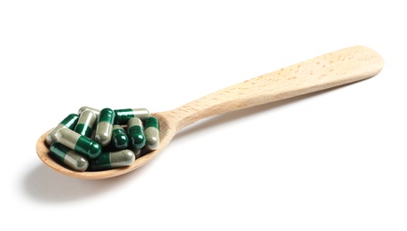 Photo of Wooden spoon with green spirulina capsules on white background