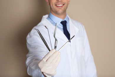 Photo of Male dentist holding professional tools on color background, closeup
