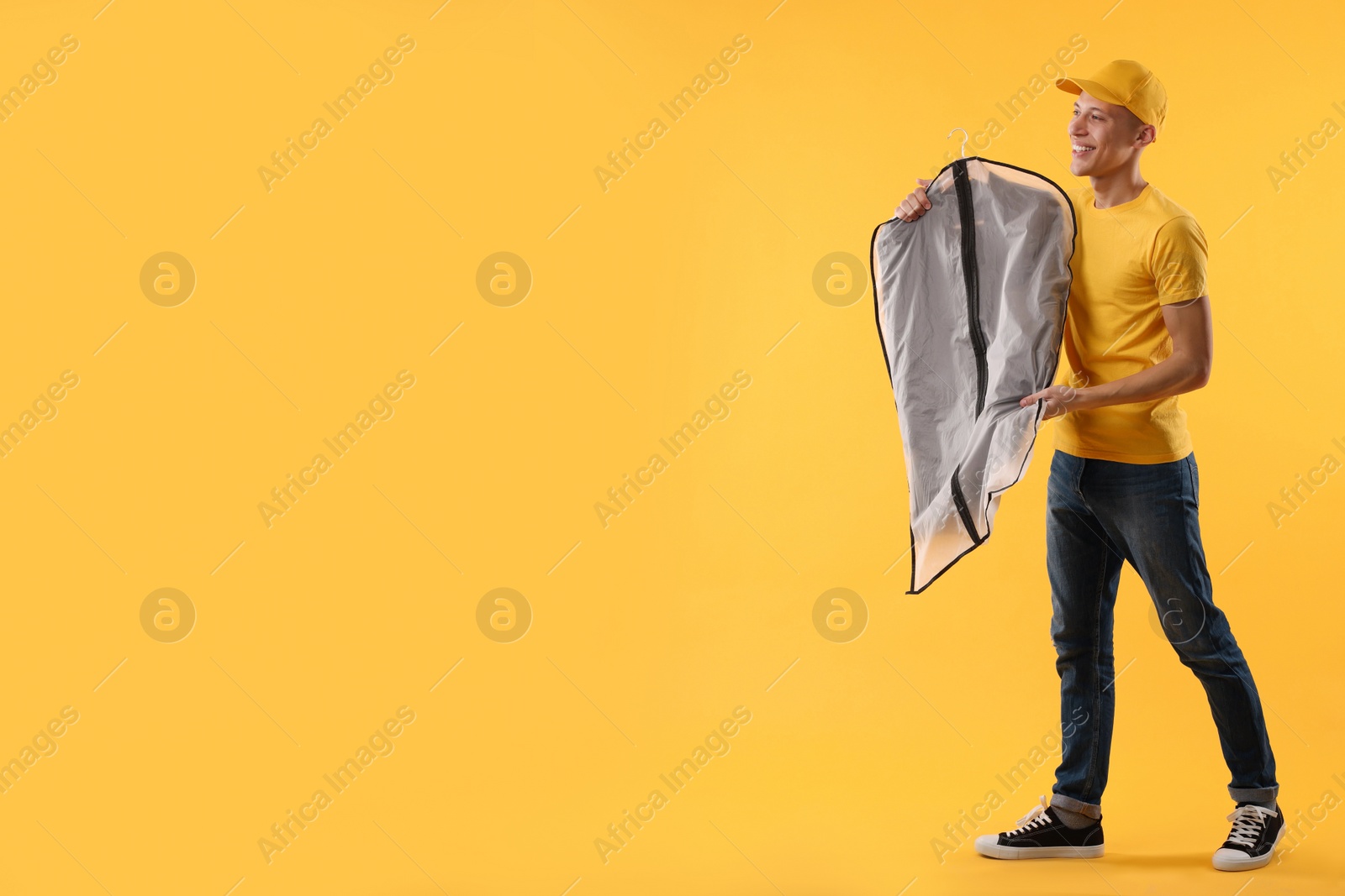 Photo of Dry-cleaning delivery. Happy courier holding garment cover with clothes on orange background, space for text