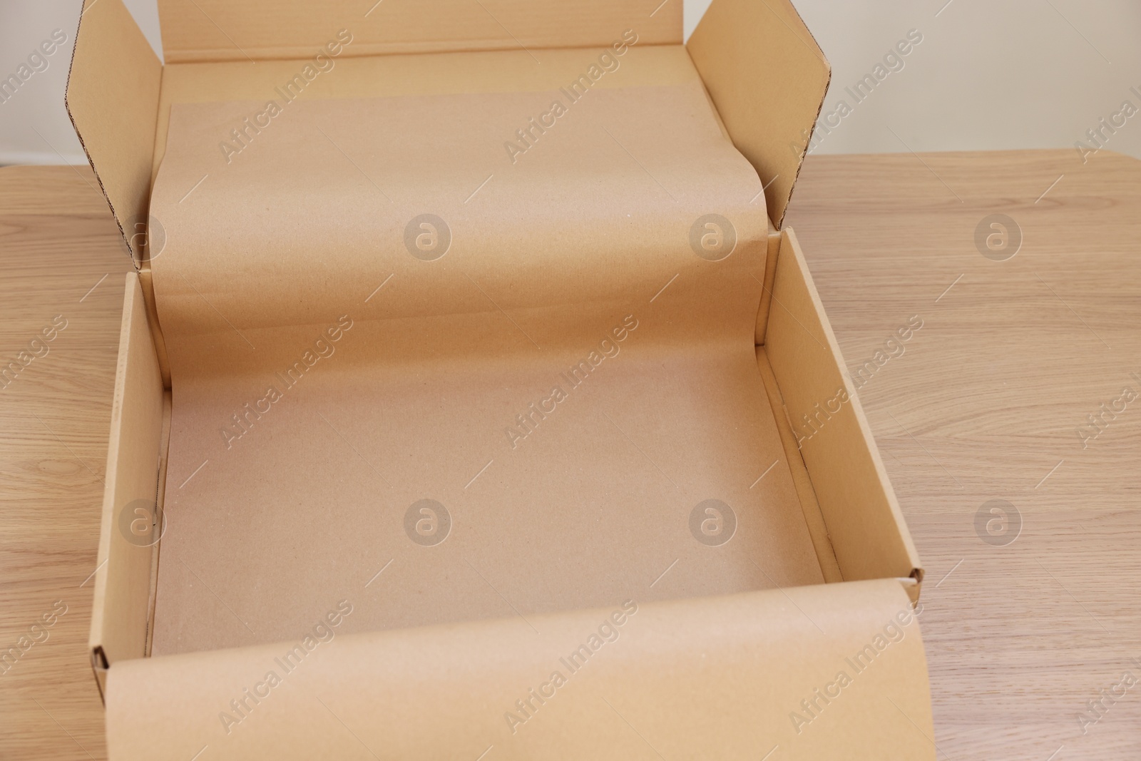 Photo of Empty cardboard box with kraft paper on wooden table, closeup. Delivery service