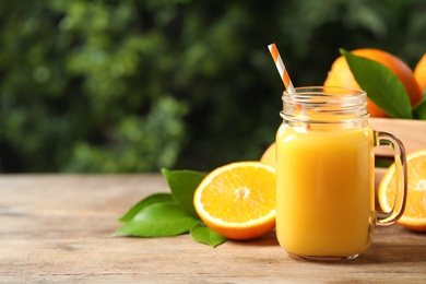 Photo of Mason jar of orange juice and fresh fruits on wooden table. Space for text