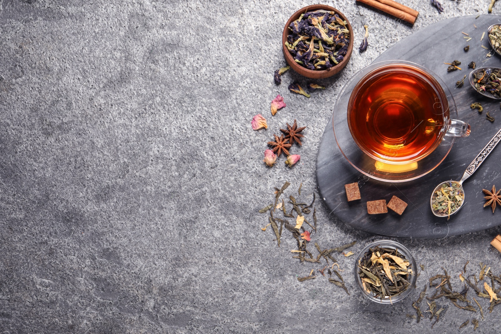 Photo of Flat lay composition with freshly brewed tea and dry leaves on grey table. Space for text