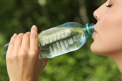 Beautiful young woman drinking water outdoors, closeup. Refreshing drink