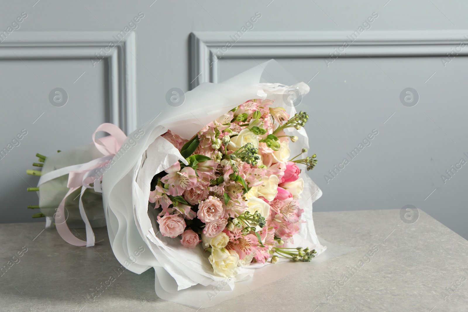 Photo of Beautiful bouquet of fresh flowers on table near grey wall, space for text