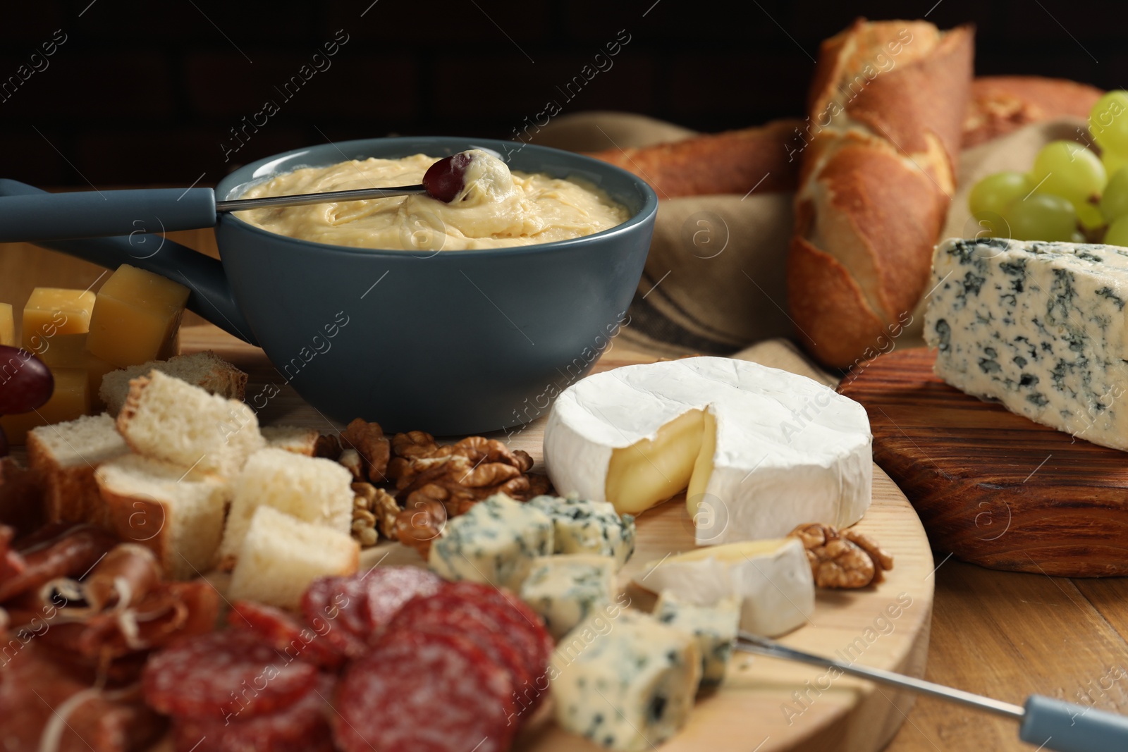 Photo of Fondue pot with tasty melted cheese, forks and different snacks on wooden table