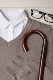 Photo of Elegant walking cane, sweater and glasses on white wooden table, flat lay