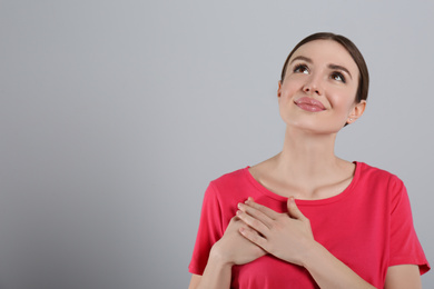 Beautiful grateful woman with hands on chest against light grey background. Space for text