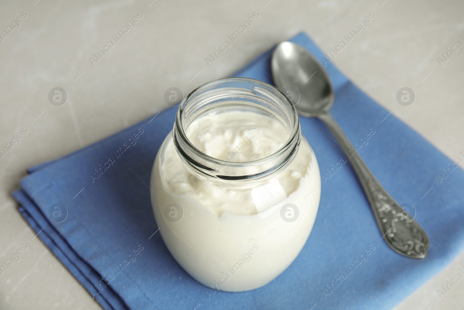 Photo of Tasty organic yogurt in glass jar on grey table