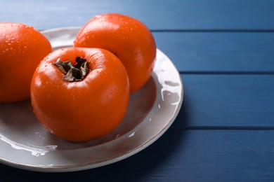 Delicious ripe persimmons on blue wooden table , closeup. Space for text