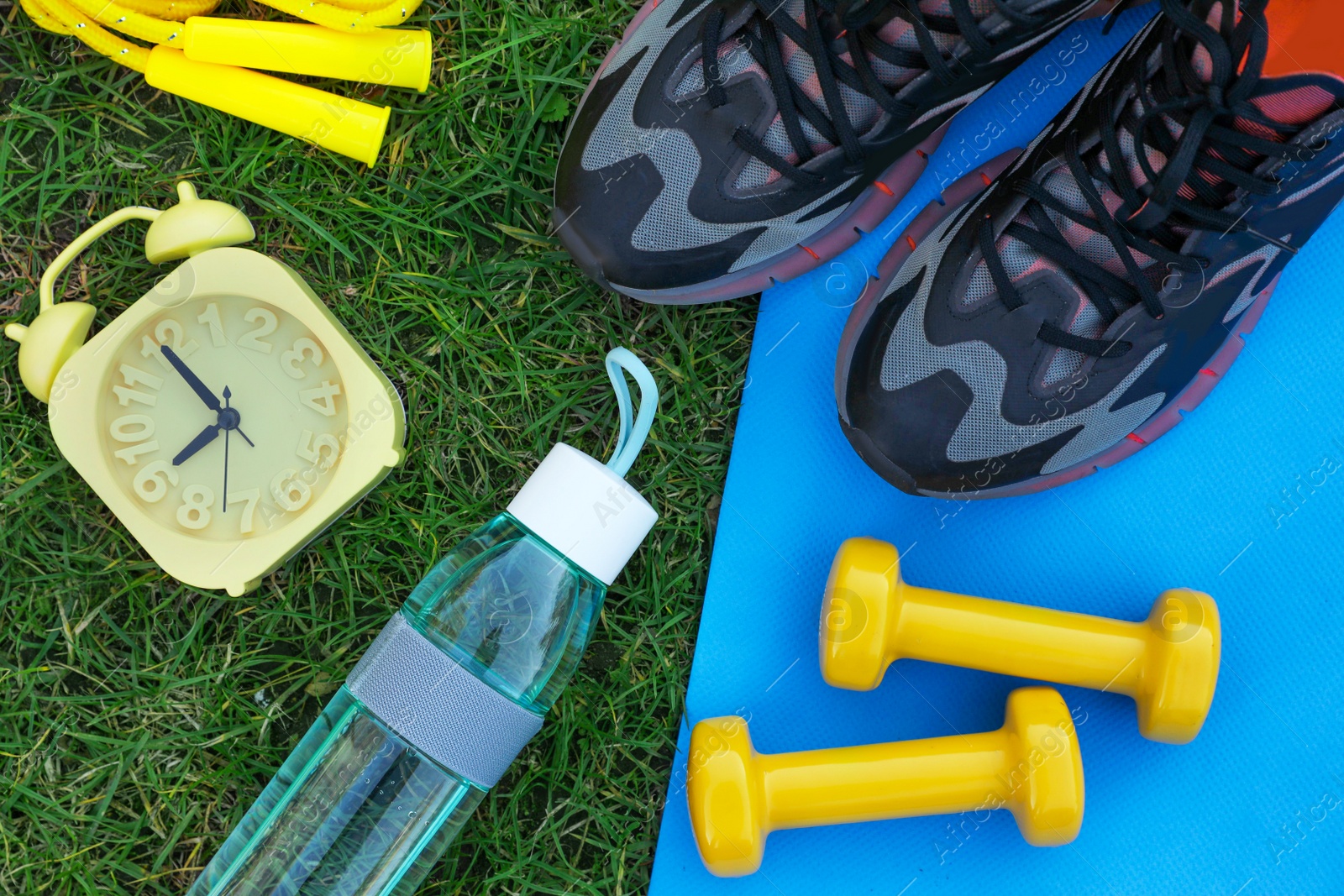 Photo of Alarm clock and set for morning exercise on green grass, flat lay