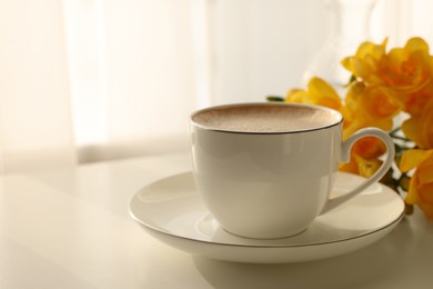 Photo of Delicious morning coffee and flowers on white table indoors, space for text