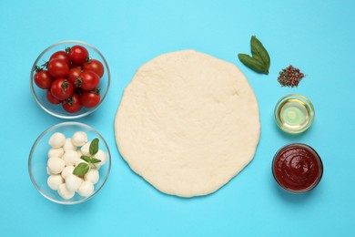 Photo of Raw dough and other pizza ingredients on light blue background, flat lay. Space for text