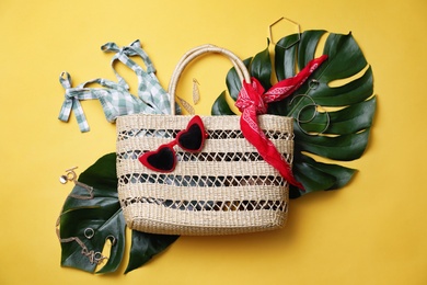 Stylish straw bag and summer accessories on yellow background, flat lay