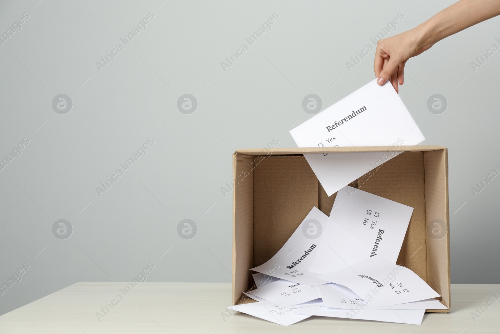 Photo of Woman putting referendum ballot in box on table against light grey background, closeup. Space for text