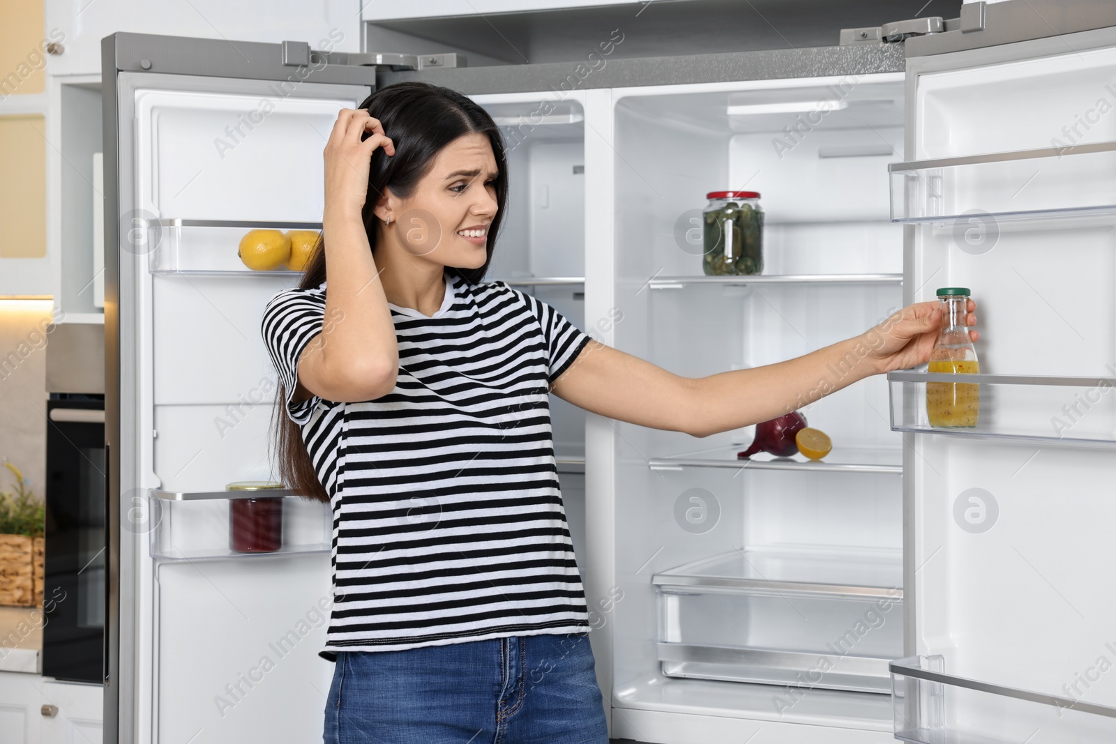 Photo of Upset woman near empty refrigerator in kitchen