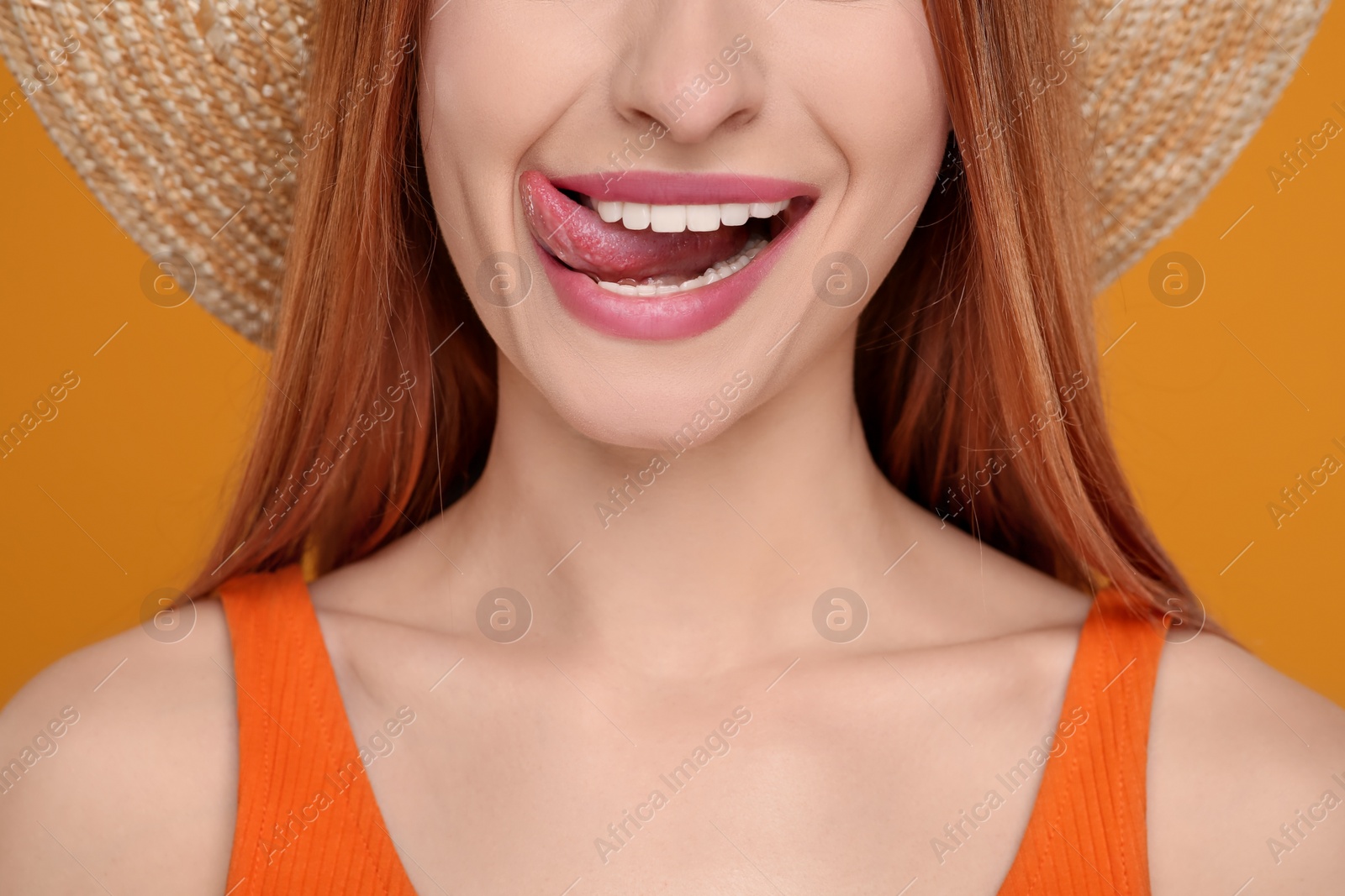 Photo of Happy woman showing her tongue on orange background, closeup