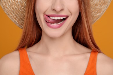 Happy woman showing her tongue on orange background, closeup