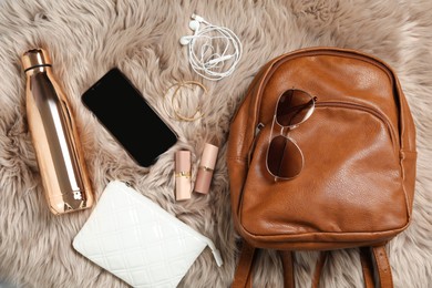 Photo of Stylish urban backpack and different items on brown faux fur, flat lay