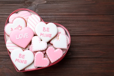 Photo of Valentine's day cookies in heart shaped box on wooden table, top view. Space for text