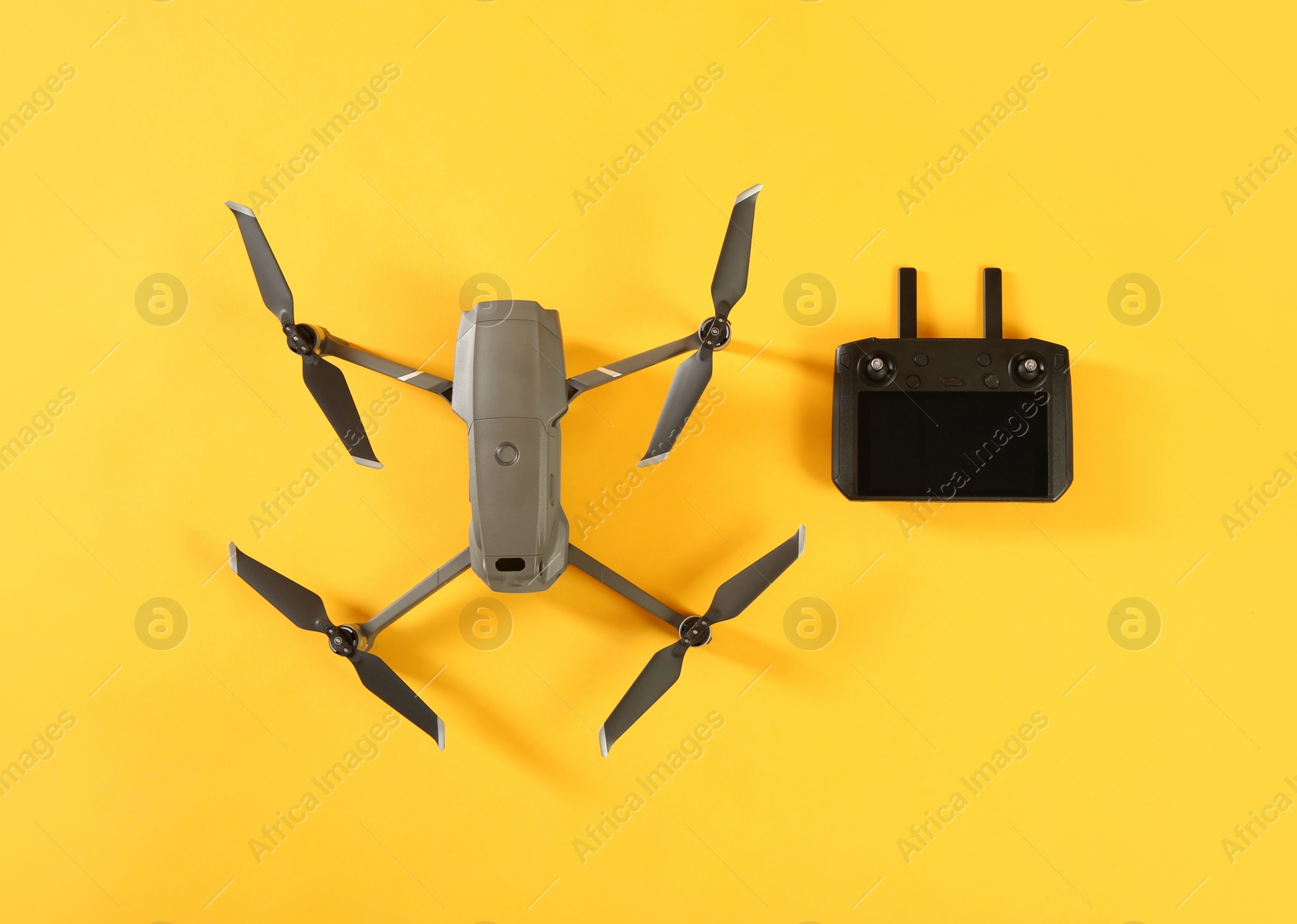 Photo of Modern drone with controller on yellow background, flat lay