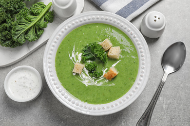 Photo of Tasty kale soup with croutons served on grey table, flat lay