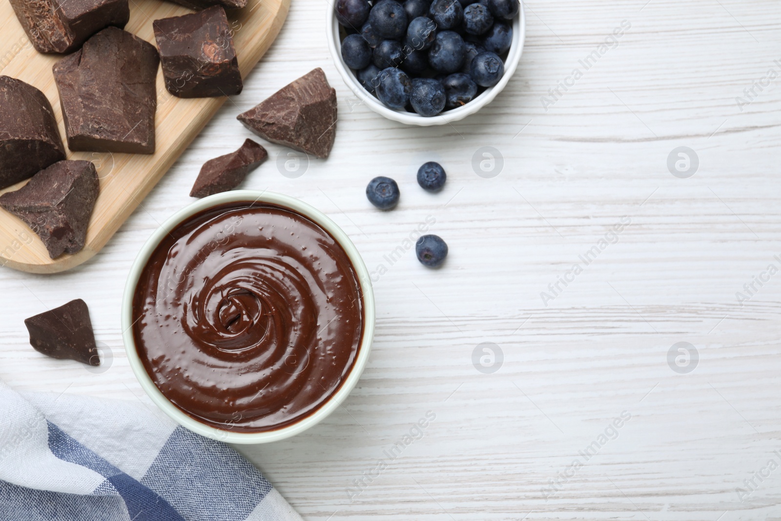 Photo of Delicious chocolate cream and blueberries on white wooden table, flat lay. Space for text