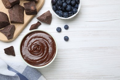 Delicious chocolate cream and blueberries on white wooden table, flat lay. Space for text