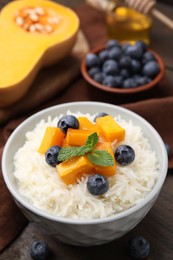 Photo of Bowl of delicious rice porridge with blueberries and pumpkin on wooden table, closeup