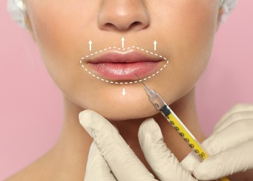 Image of Young woman getting lips injection on pink background, closeup. Cosmetic surgery